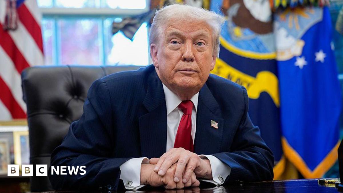 Donald Trump sitting in the Oval Office with his hands crossed