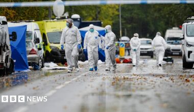 Forensics search the streets surrounding the synagogue. Three officers wear white overalls, blue gloves and face masks
