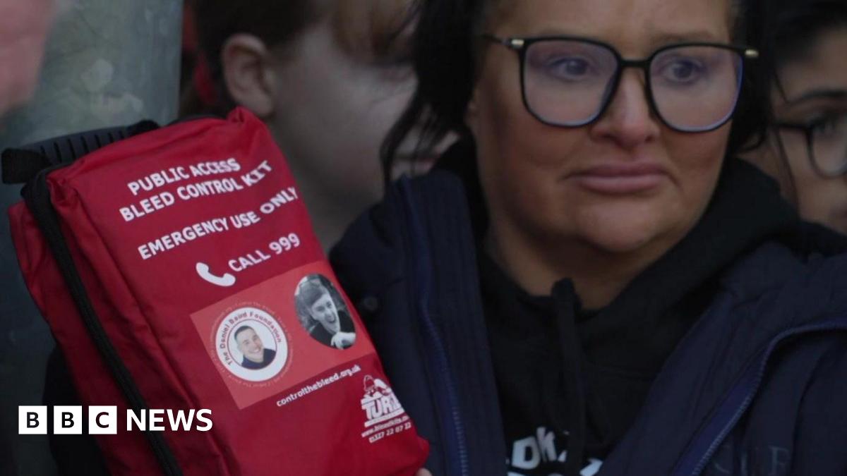 A woman wearing black-rimmed glasses holds a red package marked "bleed control" kit and which also bears a picture of Harvey Willgoose