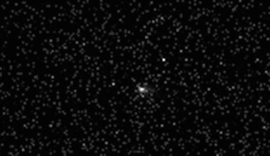 black and white photo of a comet, seen as a blurry white orb, in deep space, with fuzzy and distant stars all around