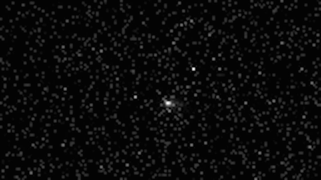 black and white photo of a comet, seen as a blurry white orb, in deep space, with fuzzy and distant stars all around