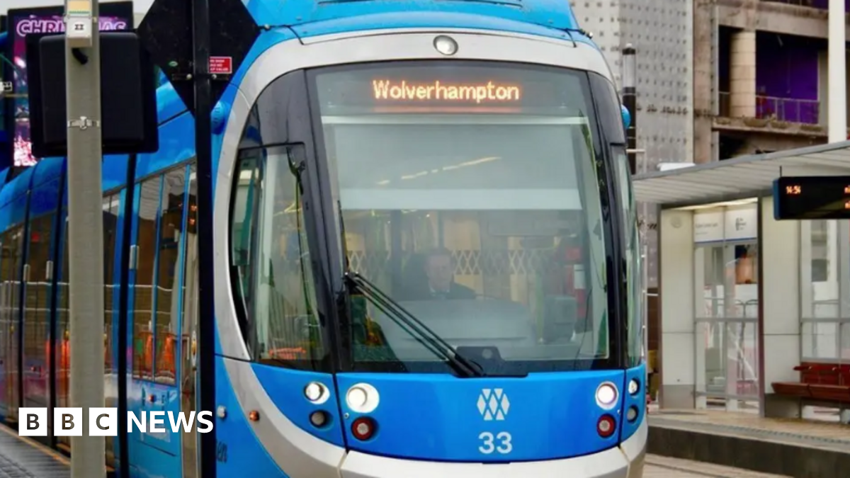 A tram navigates it way through Birmingham city centre amid major construction work with cones also laid out on roads. A person walks along a footpath to the left of the image.