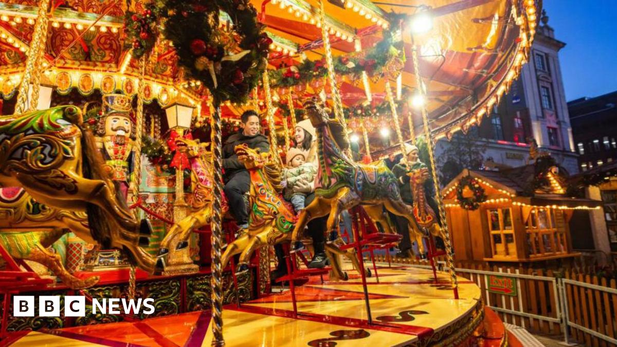 A lit up funfair roundabout as evening falls with people sitting astride tow of the ride's horses