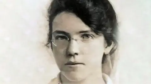 BBC A grainy picture of Jane. She has dark hair which is tied up and is wearing glasses.