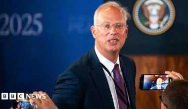 Kirill Dmitriev in a blue jacket poses for photographers in Alaska with whispy silver hair and transparent glasses