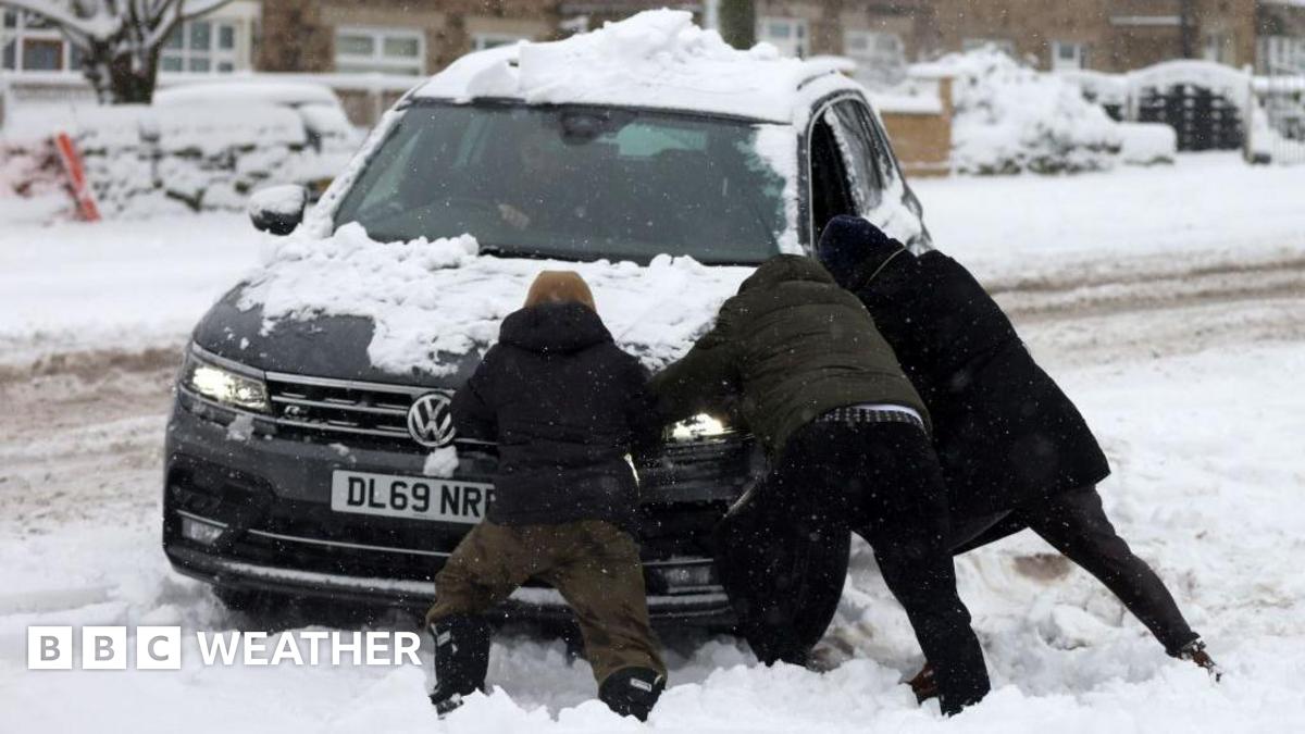heavy snow on the ground and road with three people helping to push a car that has clearly got stuck