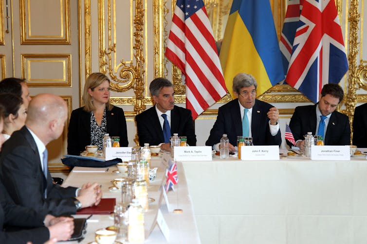 John Kerry sits around a table with other men and women in suits.