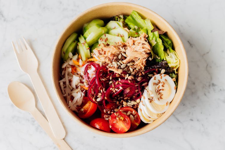Tuna fish salad with lettuce, cherry tomatoes, cucumber, egg and pickled onion in eco paper box container.
