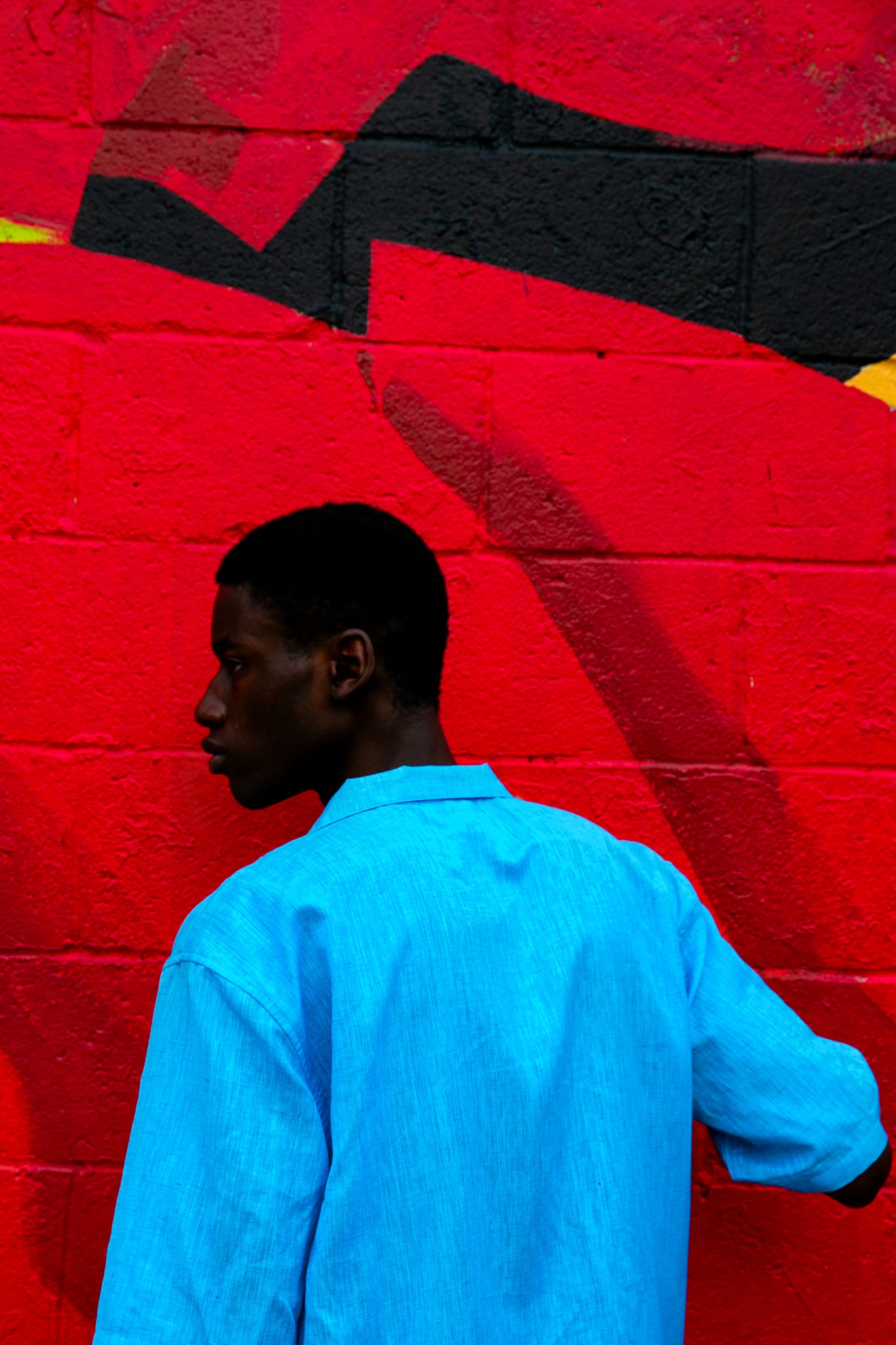 a photograph by Yannis Guibinga of a Black man wearing a light blue shirt, standing in front of a bright red wall
