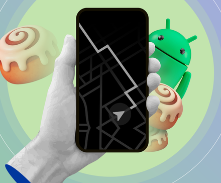 Hand holding a phone showing a minimalist map on the always-on display, with the Android mascot and cinnamon rolls in the background.