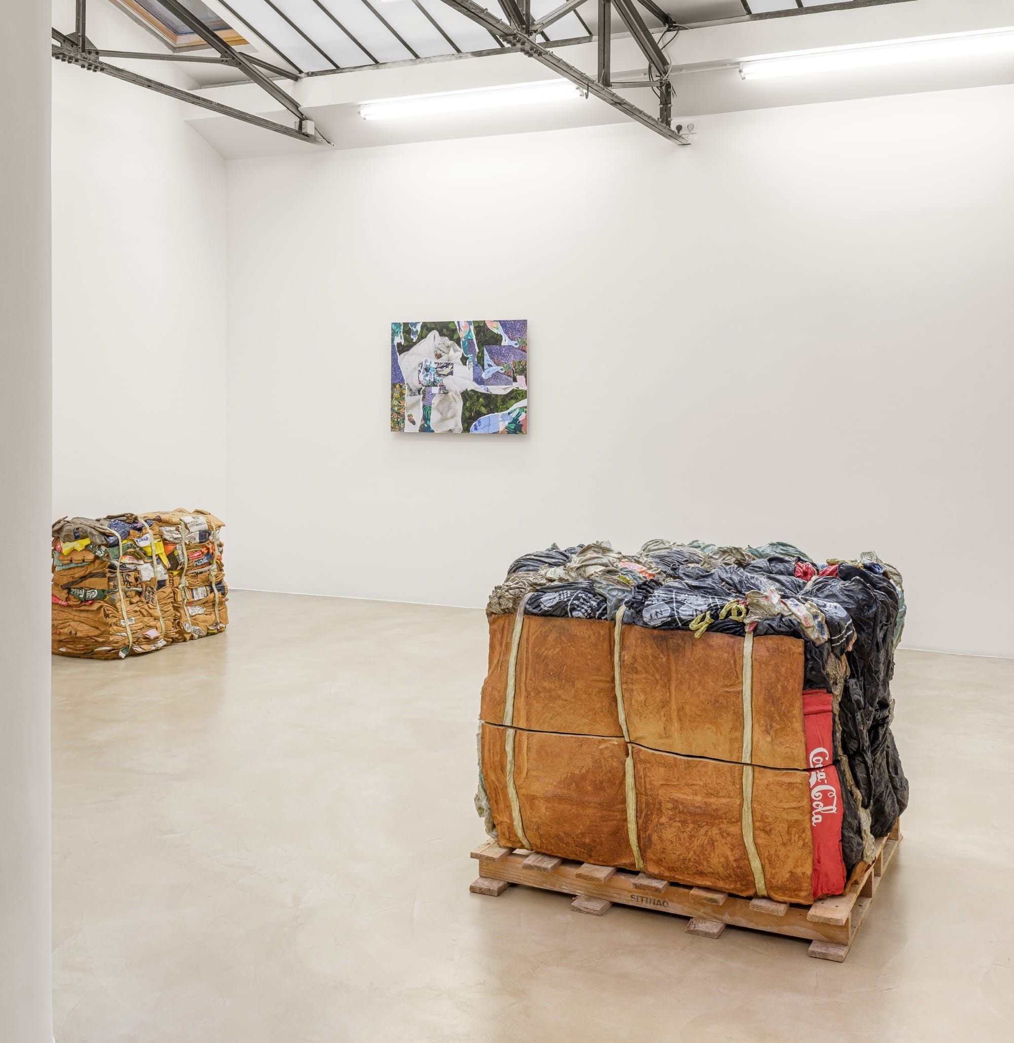 an installation view of an exhibition by Ninon Hivert of glass, bronze, and clay sculpture mimicking stacks of discarded materials like cardboard and clothing