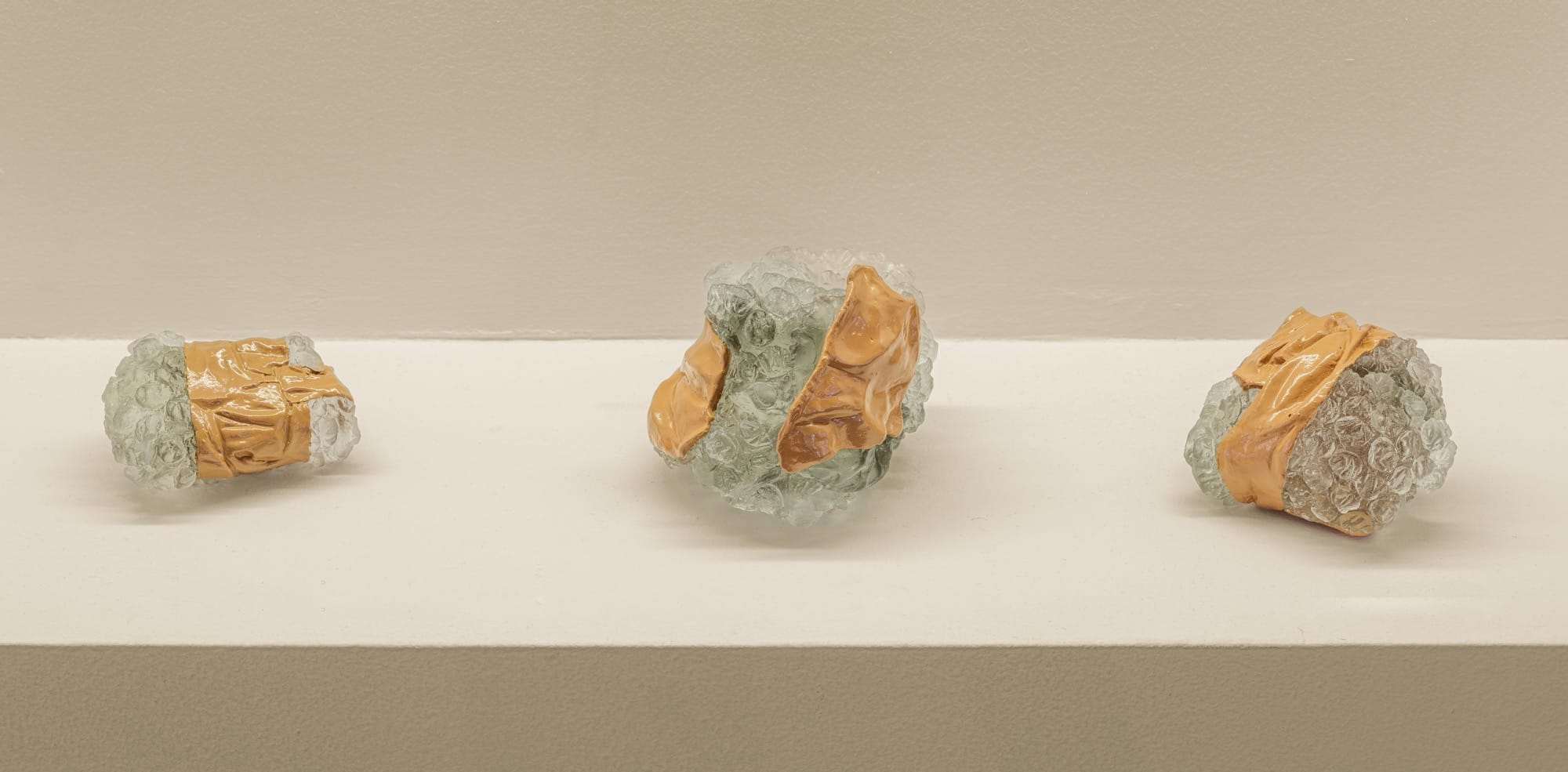 three glass sculptures by Ninon Hivert of bubble-wrapped parcels with packing tape