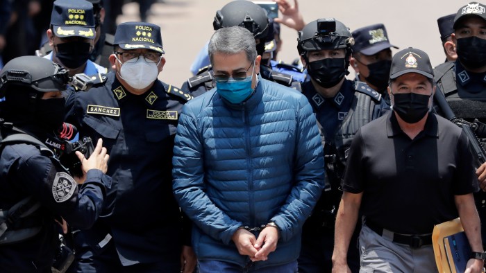 Juan Orlando Hernandez, wearing handcuffs and a blue jacket, is escorted by police special forces officers in Tegucigalpa