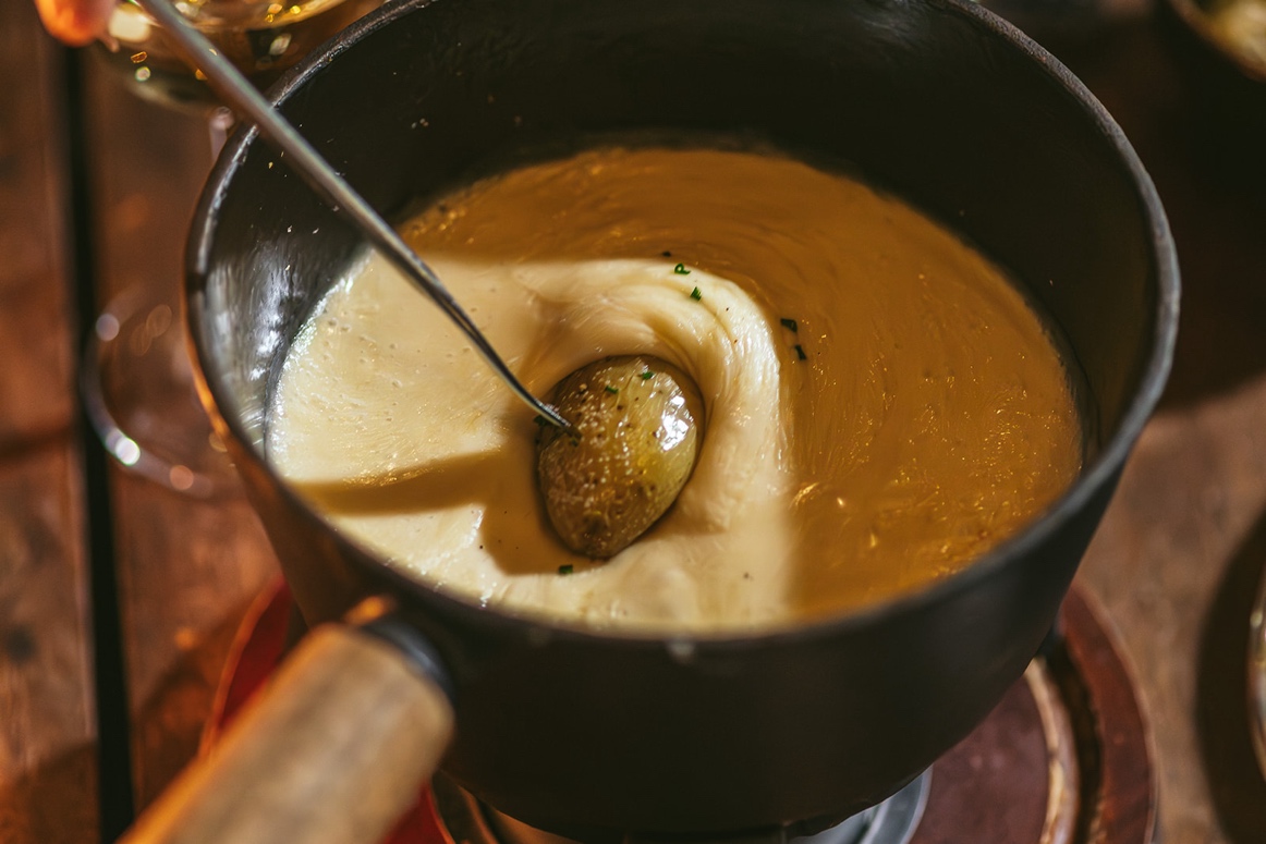 a potato on a skewer being dipped into a thick pot of fondue