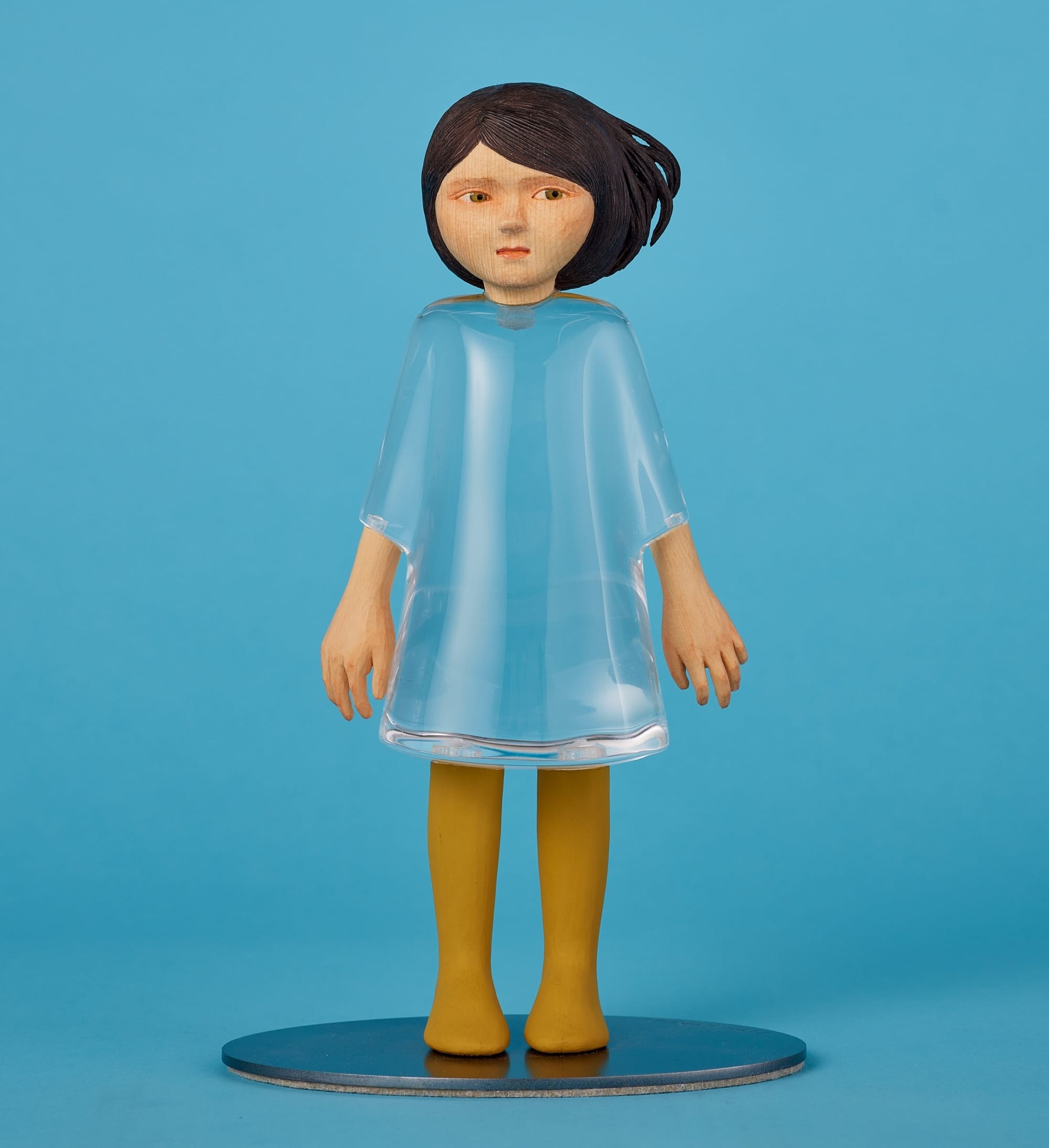 a small sculpture by Ayako Kita made of cypress and acrylic resin, depicting a young woman with a dress made of clear material so that we can see right through her