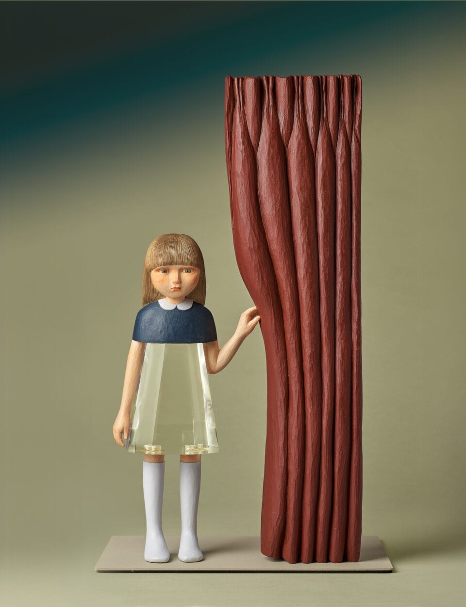 a small sculpture by Ayako Kita made of cypress and acrylic resin, depicting a young woman standing beside a large red curtain