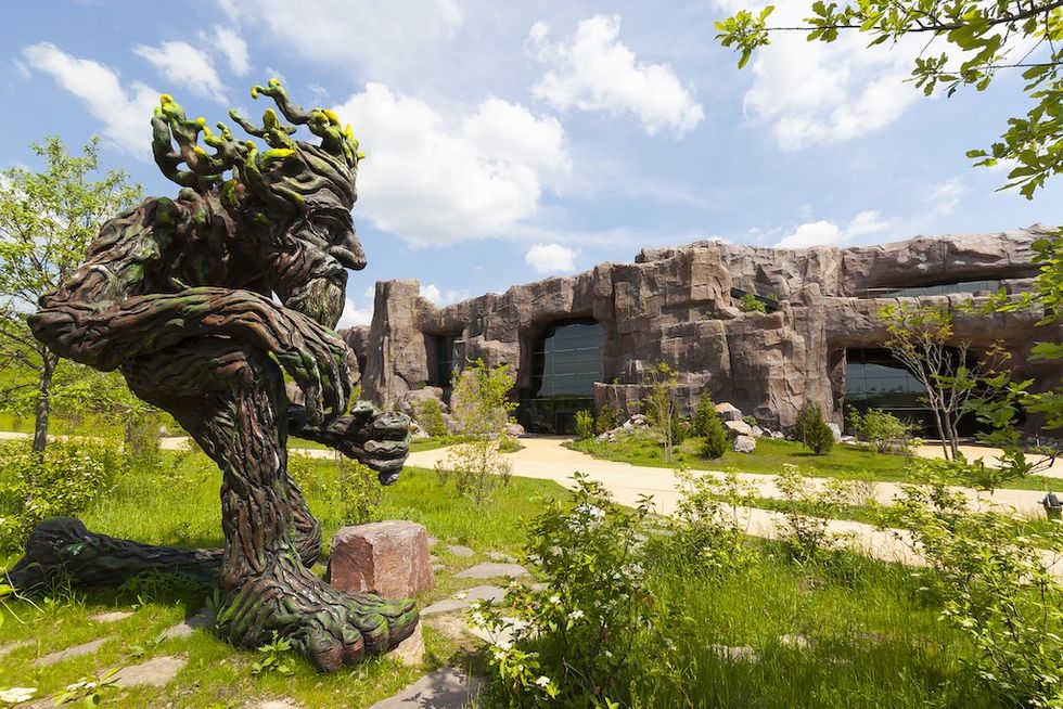 Large tree-like sculpture in a garden with a rocky building background under a blue sky.