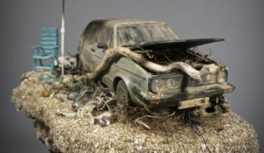 a hand-sculpted miniature by Simon Laveuve of an abandoned car with a large root growing through the hood, with a beach umbrella propped up next to it