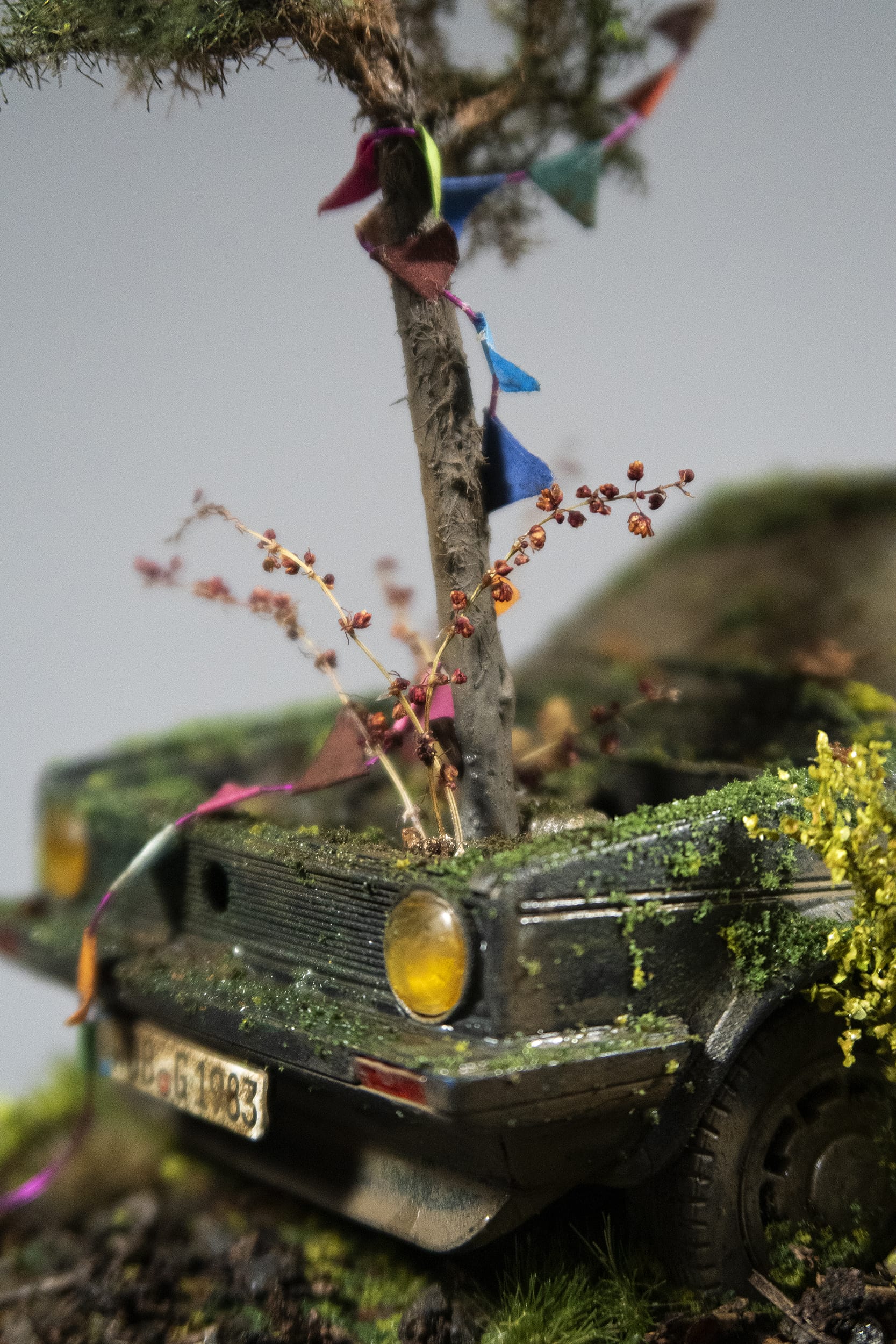a detail of a hand-sculpted miniature by Simon Laveuve of an abandoned car with a tree growing out of the hood