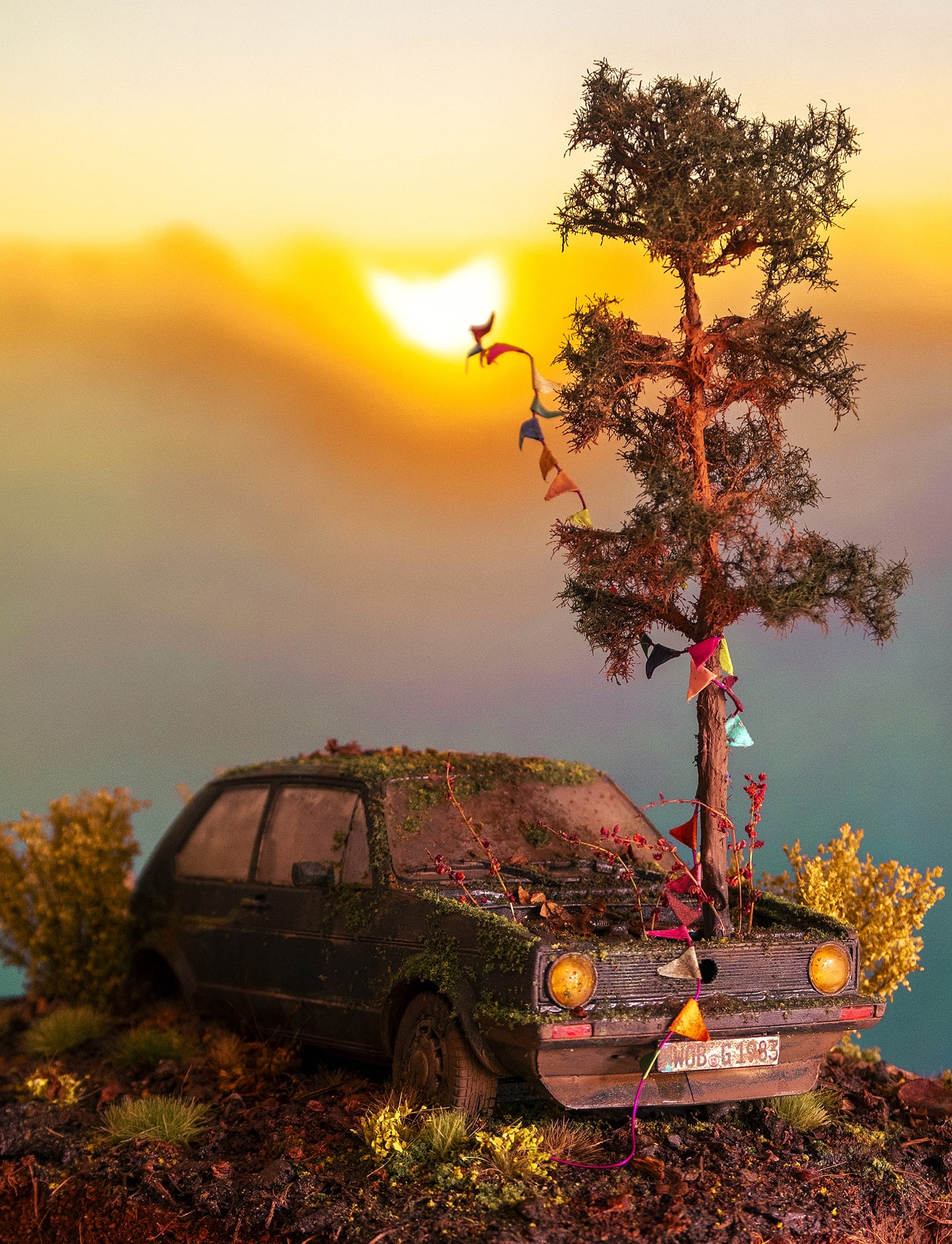 a hand-sculpted miniature by Simon Laveuve of an abandoned car with a tree growing out of the hood, set against a sunrise