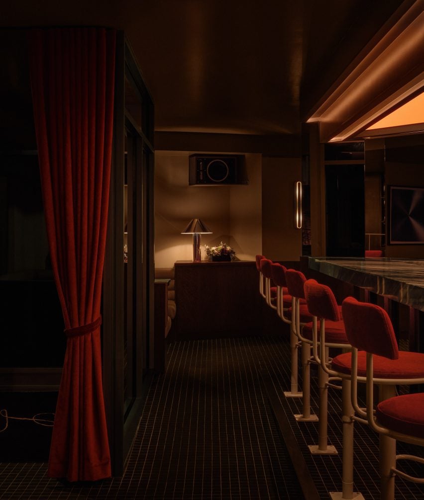 Bar interior with red velvet curtains on one side and a row of stools on the other