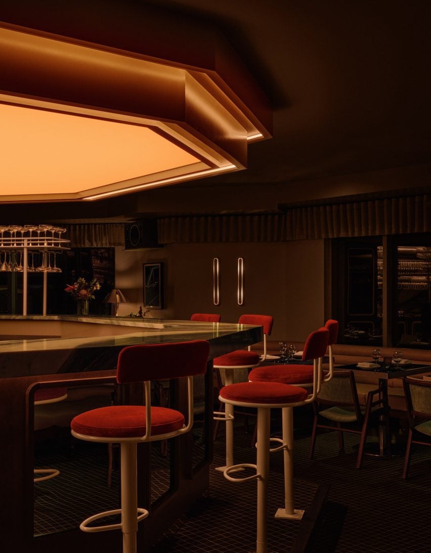 Diamond-shaped bar with a lightbox above and red velvet stools surrounding