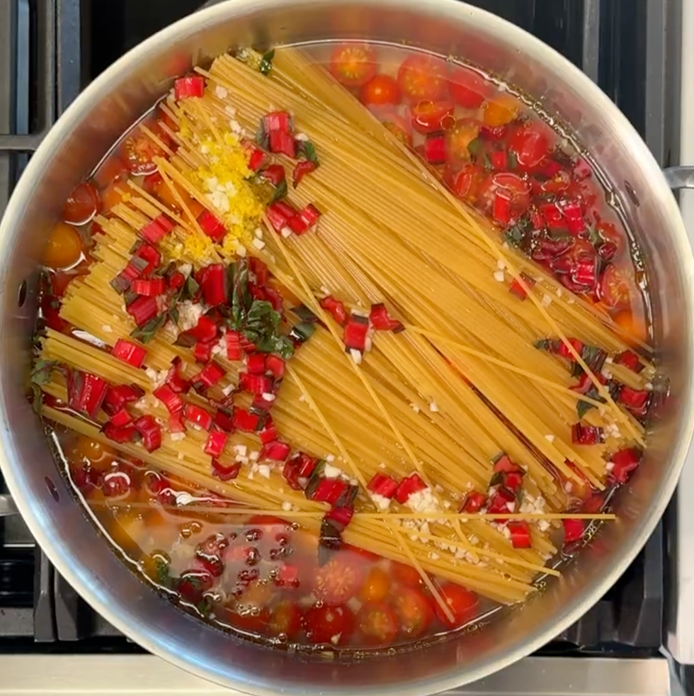 uncooked spaghetti and tomatoes in a skillet with boiling water on top