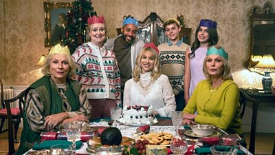A group of people sit and stand around a table set for Christmas dinner, smiling