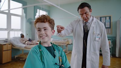 Image from the upcoming adaptation Dexter Procter. Cian Eagle-Service and Peter Serafinowicz are dressed as doctors on a hospital ward.