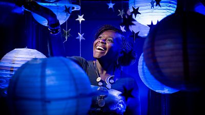 A woman smiles as she looks upward through a selection of spherical lamp shades and hanging stars, imitating the galaxy