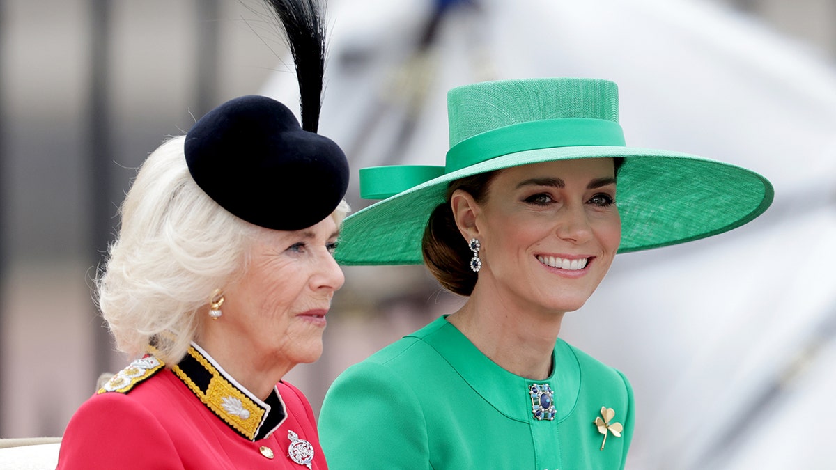 Queen Camilla and Kate Middleton sitting next to each other on a royal carriage outdoors in formal wear.