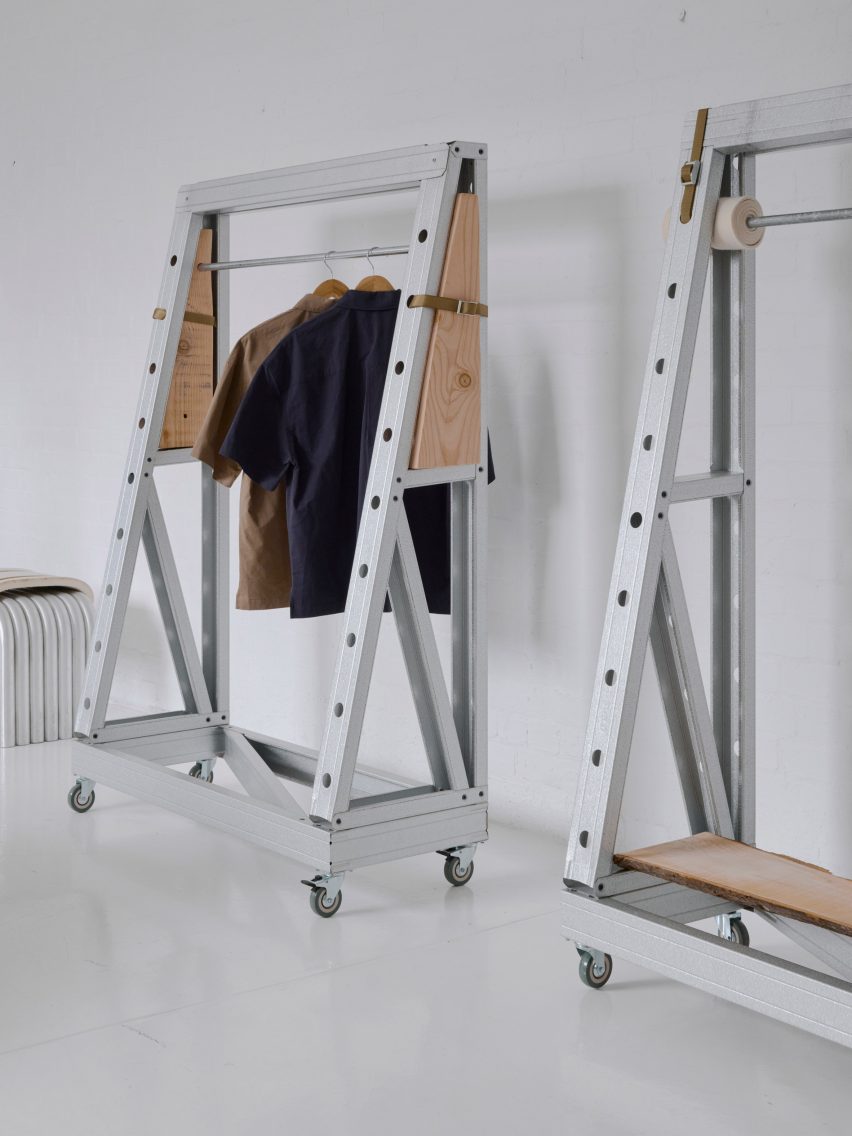 Minimalist clothing rack setup with industrial steel frames and wooden panels on caster wheels, displaying neutral-toned shirts on hangers in a white studio space.