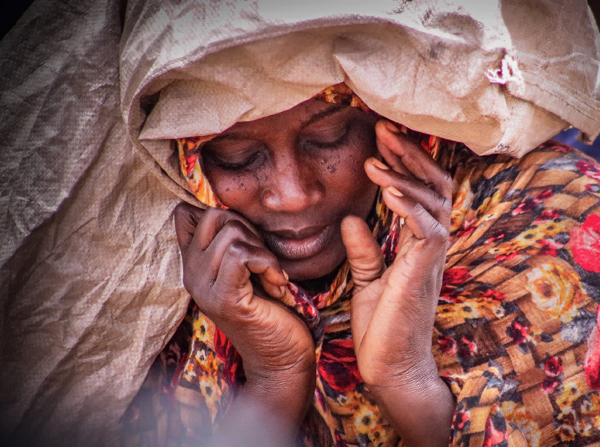 a portrait photo by Abdelsalam Abd Allah of a woman with a scarf around her head and her hands near her face as she looks down
