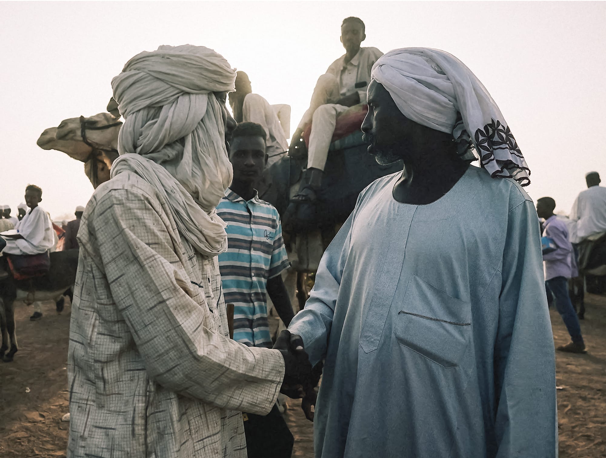 a photo by Mohamed Zakaria of two men wearing robes and turbans, shaking hands
