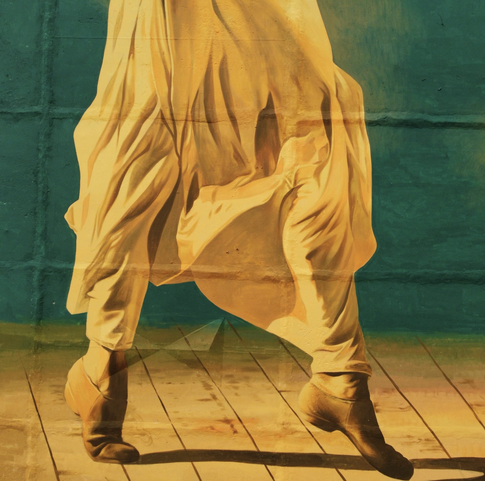 a detail of a tall mural on the side of a building of a woman dancing in a bright yellow outfit against a green background