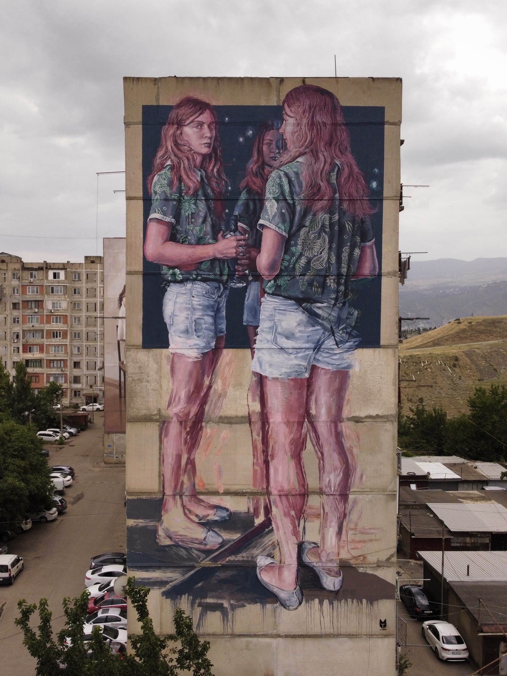 a tall mural on the side of a building of three identical women figures facing each other as if reflected in a mirror