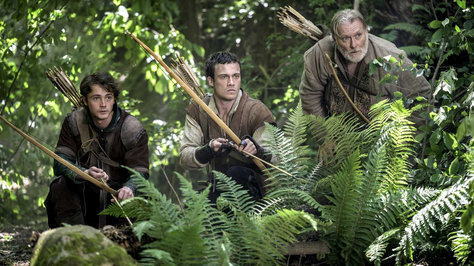 Henry Rowley, Jack Patten as Robin Hood, and Ian Pirie kneeling behind greenery while armed with bows and arrows in Robin Hood (2025)