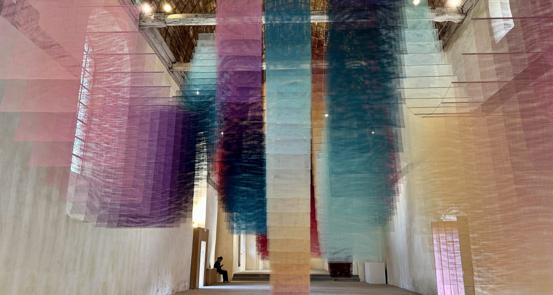 an art installation by Tomislav Topić of layers of colorful planes of fabric suspended from the ceiling in undulating rows so that it looks prismatic