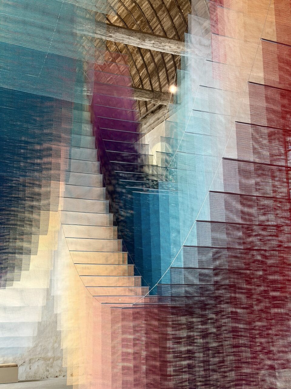 an art installation by Tomislav Topić of layers of colorful planes of fabric suspended from the ceiling in undulating rows so that it looks prismatic