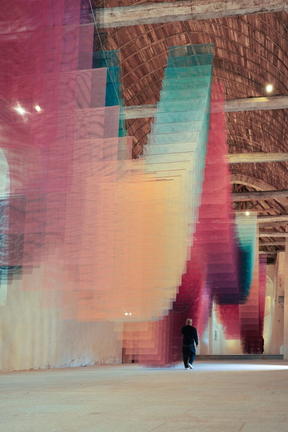 an art installation by Tomislav Topić of layers of colorful planes of fabric suspended from the ceiling in undulating rows so that it looks prismatic