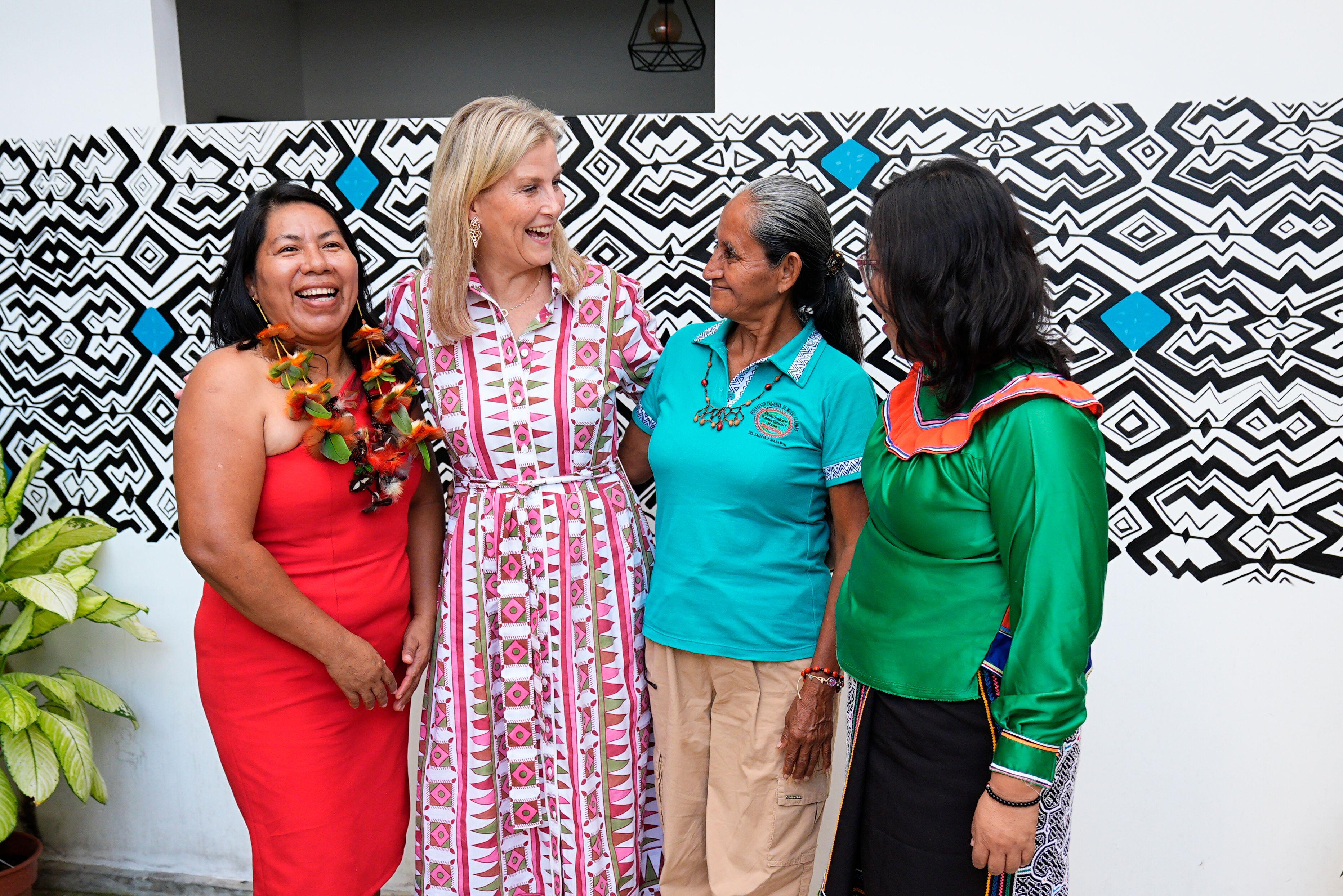 Duchess Sophie wearing a printed dress with her arms around 3 ladies and laughing