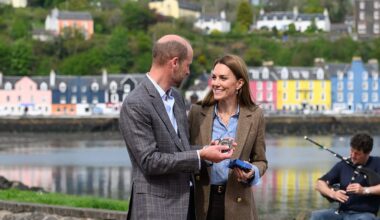 Prince and Princess of Wales with colourful houses and a bagpiper behind them in Tobermory