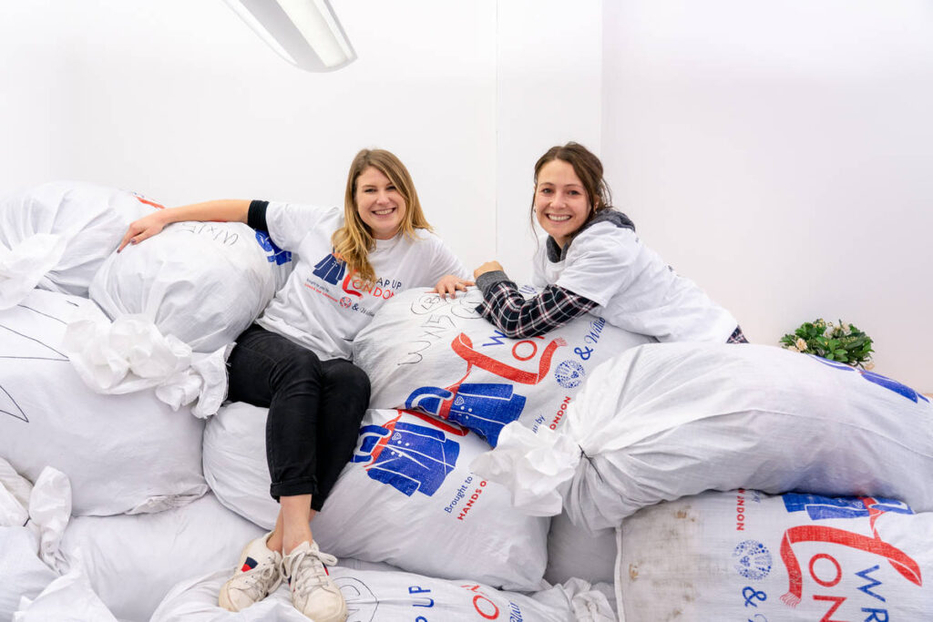 two volunteers perched atop a pile of enormous sacks of donated winter coats