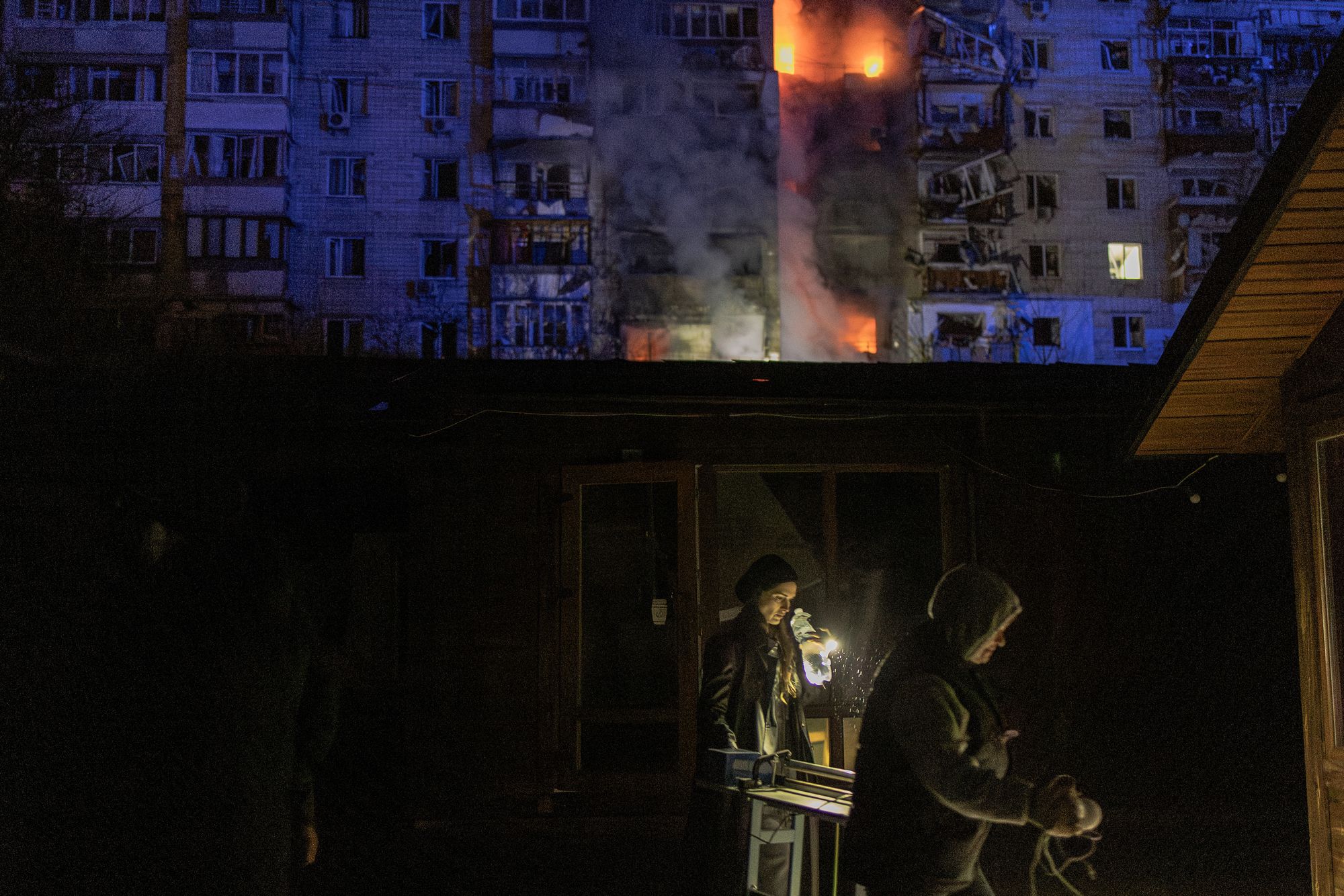 People walk past damaged shops in front of a residential building on fire following a Russian drone attack on the city of Vyshhorod, in the Kyiv region early on 30 November 2025