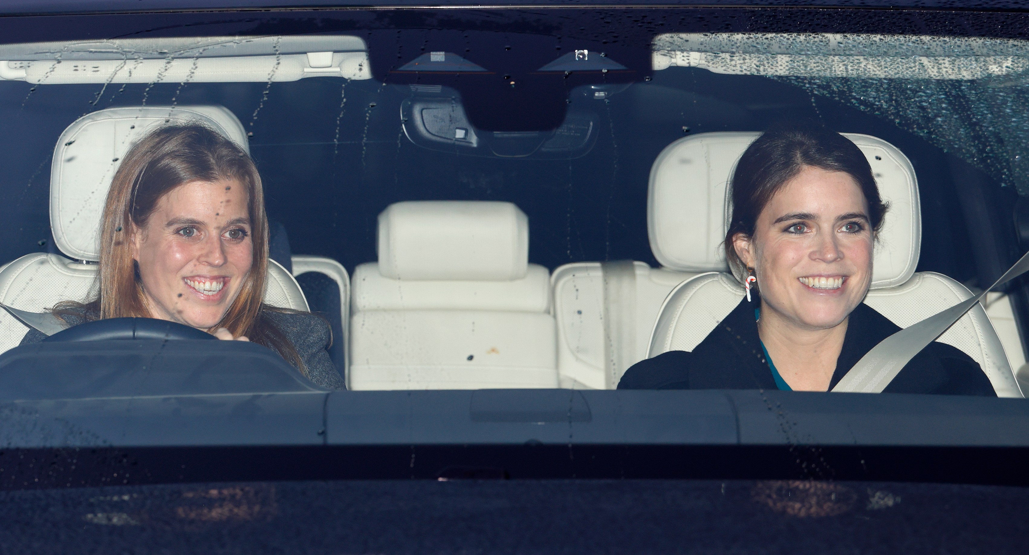 Princess Beatrice and Princess Eugenie smiling in a car.