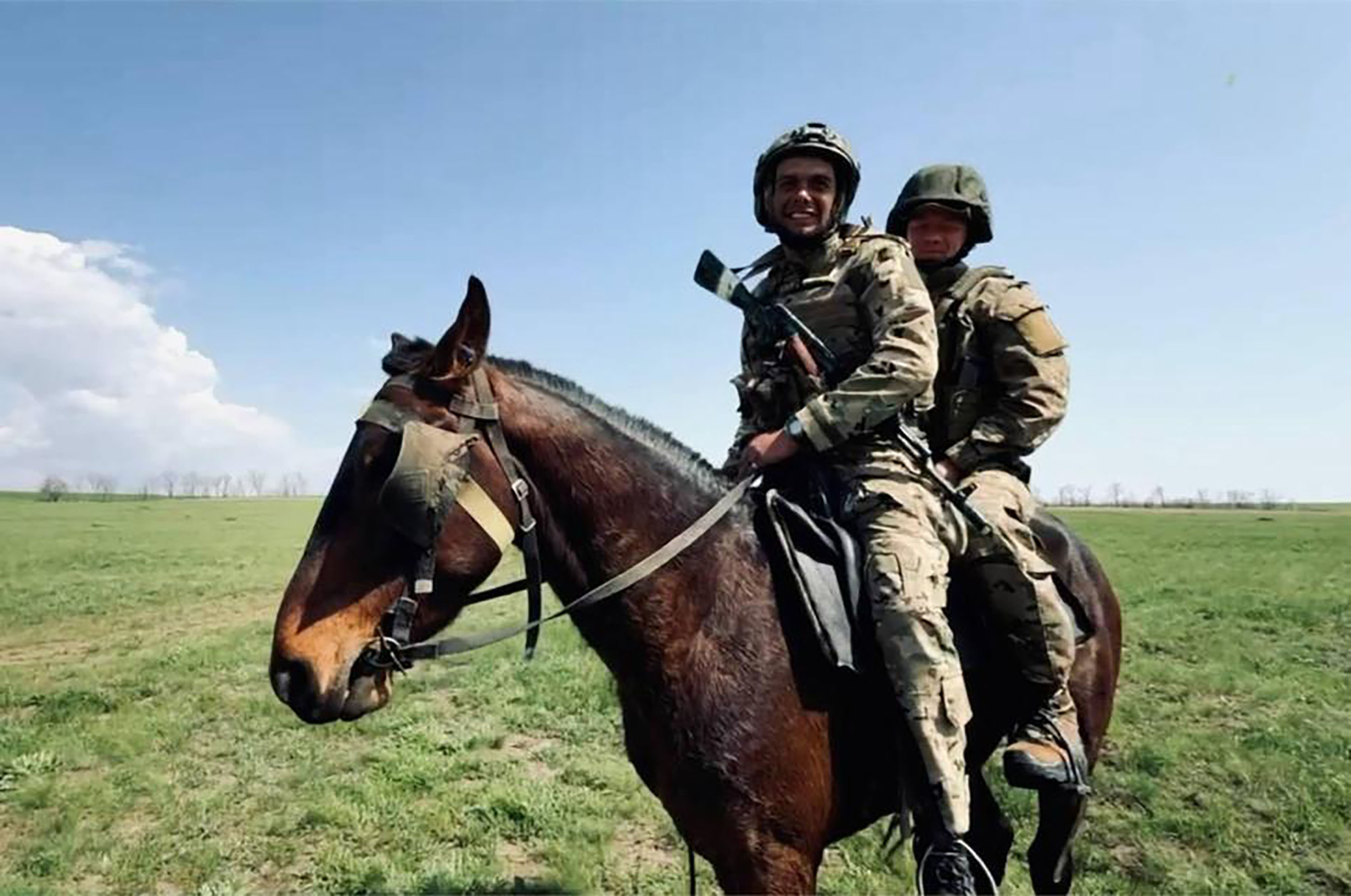 Two soldiers in camouflage and helmets ride a brown horse.