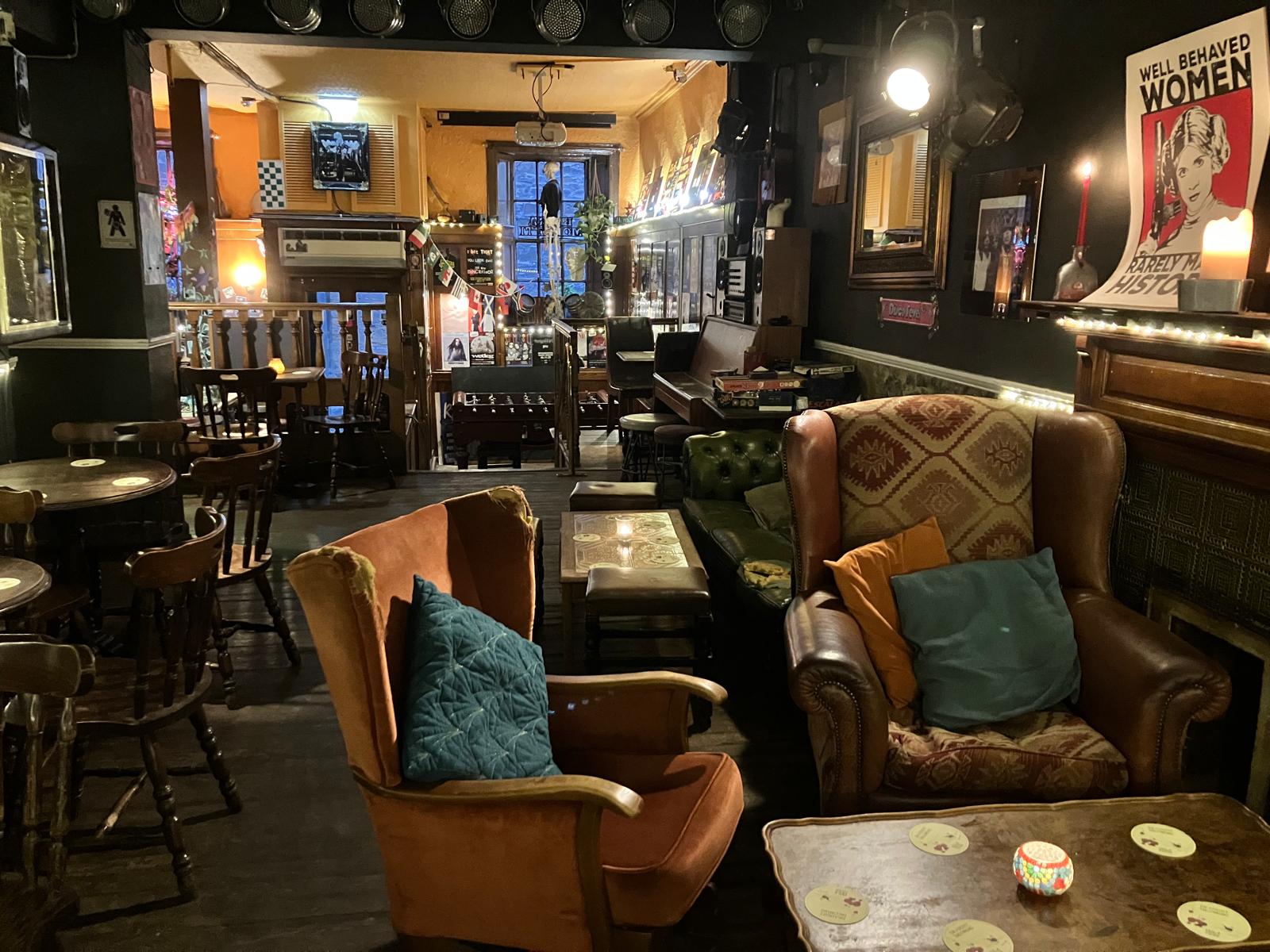 The cozy interior of Star Bar in Edinburgh, featuring two armchairs with pillows in the foreground and dimly lit tables in the background.