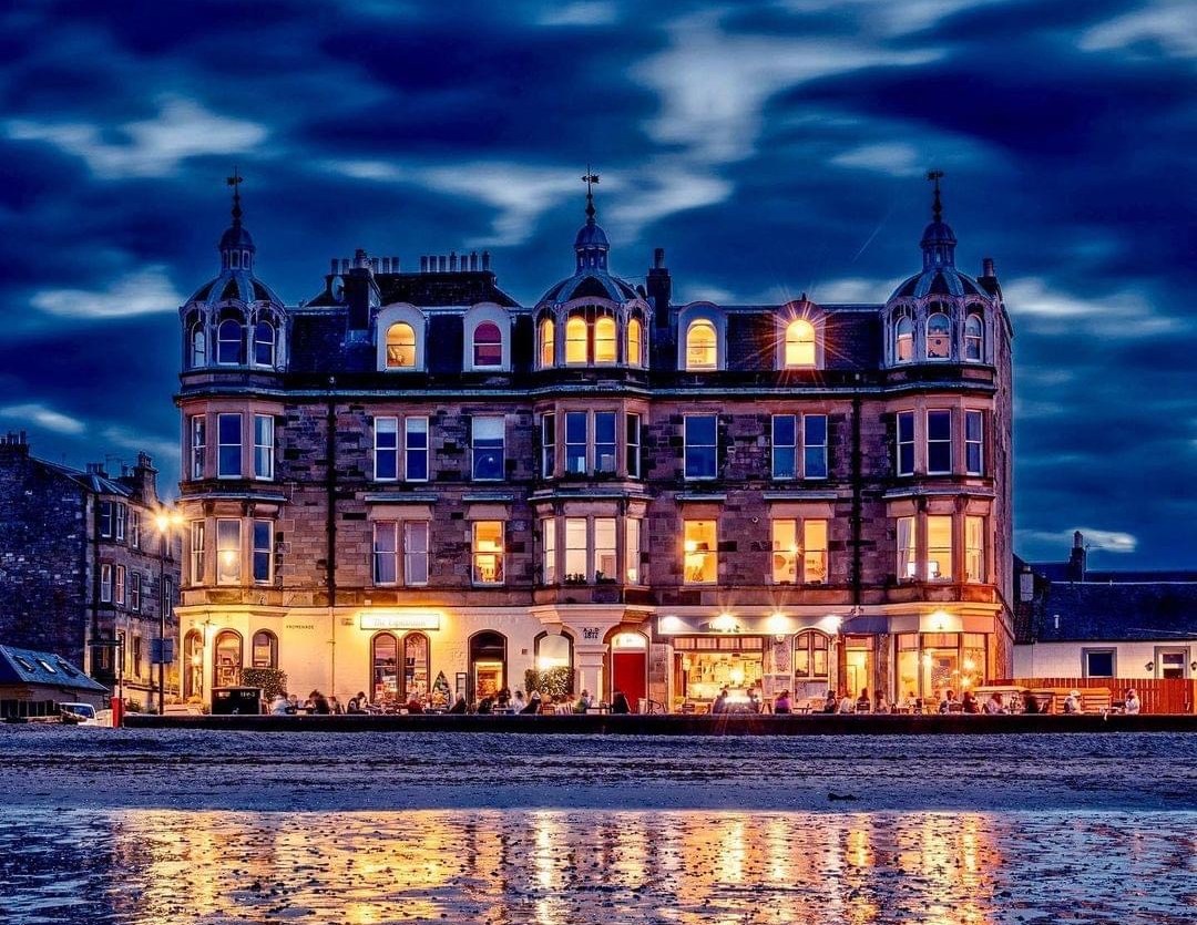 The Espy pub in Portobello at night, with lights reflecting on the wet beach sand.