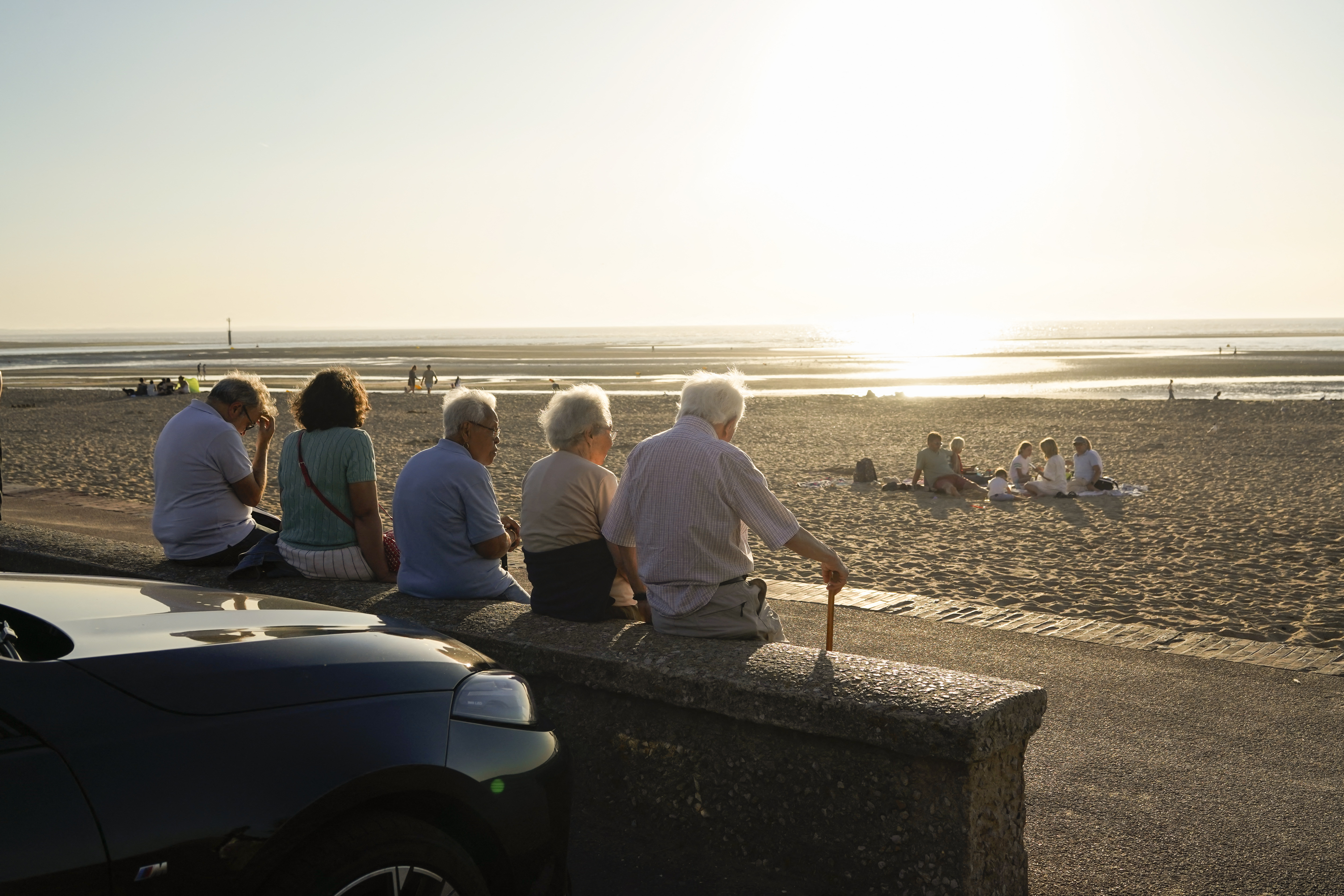 Five elderly people sitting on a concrete wall overlooking Houlgate beach in Normandy, France, as others enjoy the sand and water.