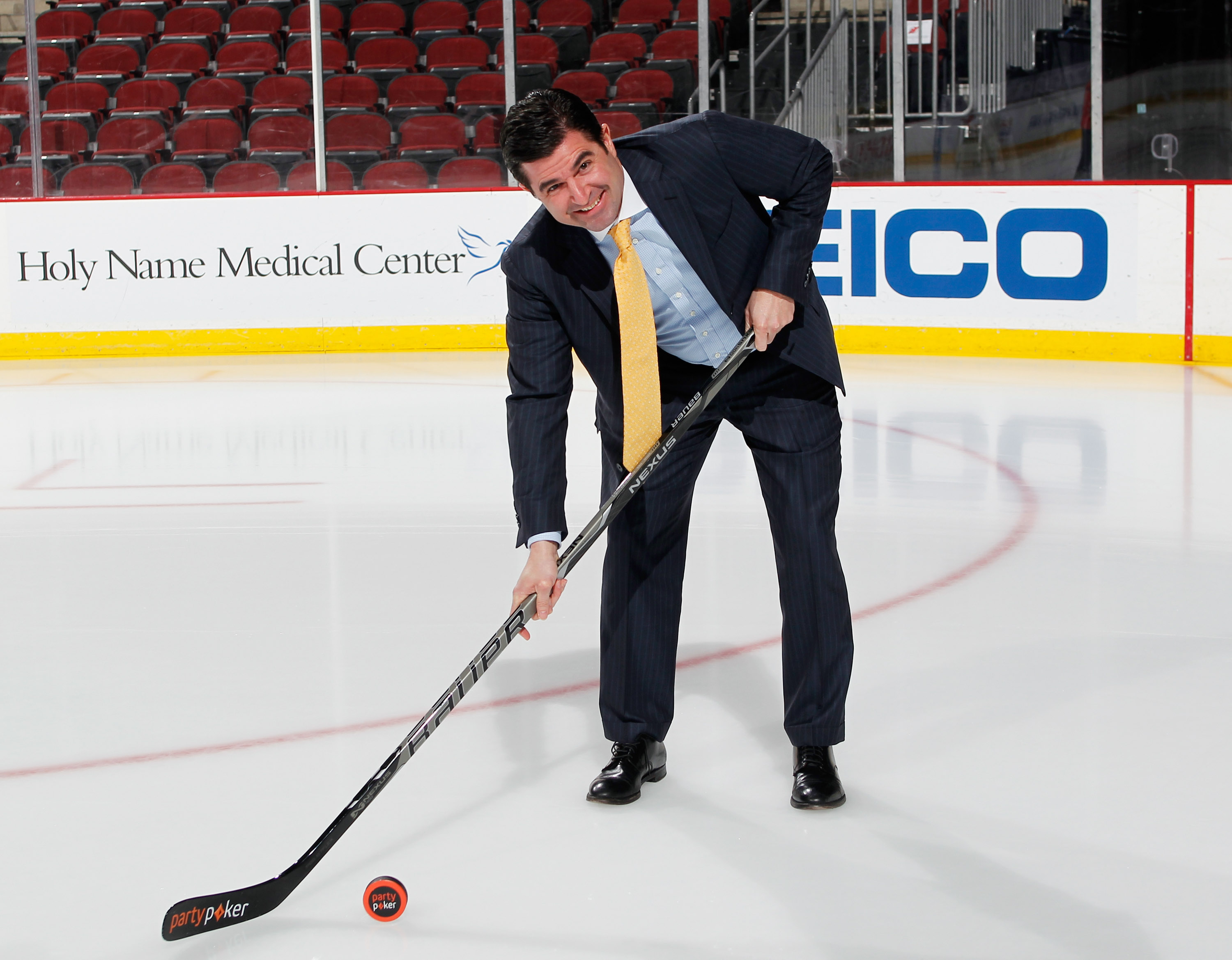 Scott O'Neil, CEO of the New Jersey Devils, Philadelphia 76ers, and Prudential Center, on ice with a hockey stick and a puck with the "partypoker" logo.